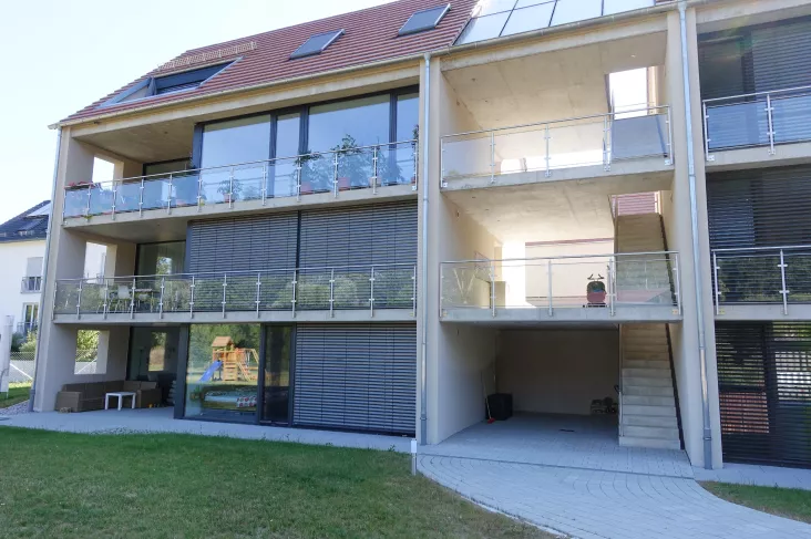 Ein Mehrfamilienhaus mit Balkonen. Diese haben ein Balkongeländer aus Glas.
